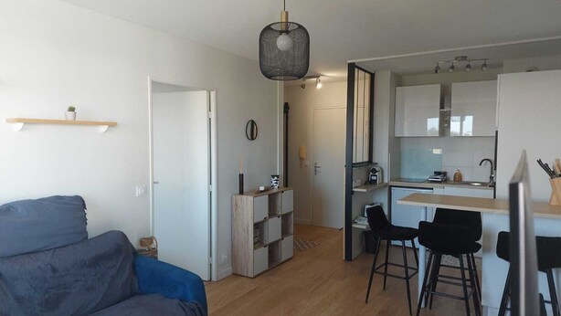 En moderne stue med sofa, spiseområde med barstol og et køkken med vask og bordplade.