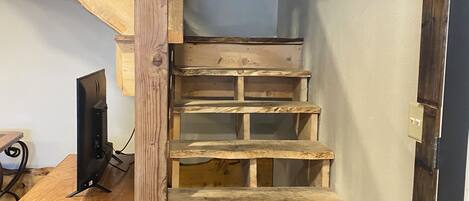A wooden staircase with a TV on a wooden desk below.