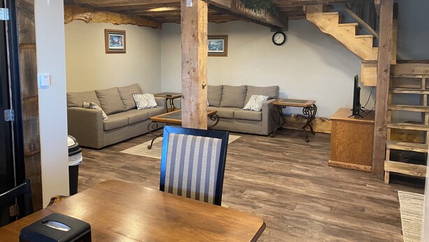 Una sala acogedora con dos sofás, una mesa de comedor de madera y una escalera.