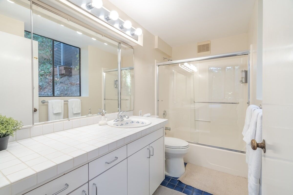 A modern bathroom with a large mirror, white tiles, a shower, and a potted plant.
