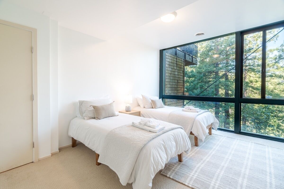 A bedroom with two beds, a large window, and a view of trees.