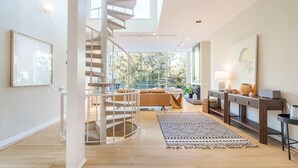 Un interior moderno con una escalera en espiral, un sofá, una mesa de centro y un ventanal con vistas a árboles.
