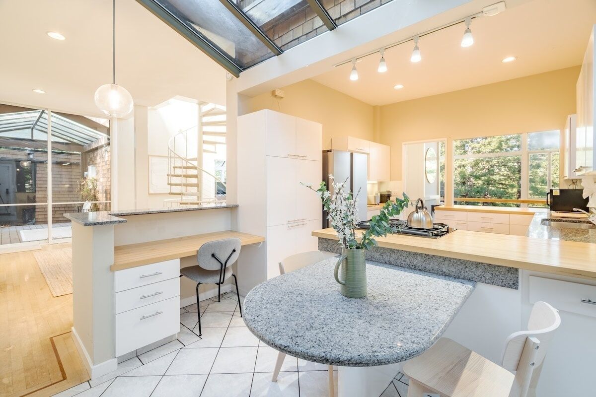 A modern kitchen with white cabinets, a granite countertop, and a dining area with a round table and chairs.