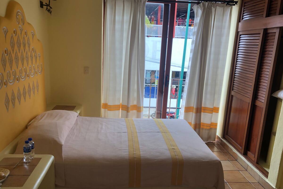 Hotelkamer met een bed, nachtkastje met telefoon en waterfles, gordijnen en uitzicht.