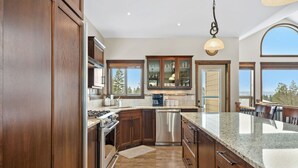 Une cuisine moderne dotée de meubles en bois, d’appareils électroménagers en acier inoxydable et de grandes fenêtres offrant une vue sur l’extérieur.