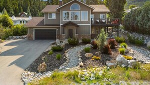 Une maison à deux étages avec un garage, entourée d’un jardin aménagé avec différentes plantes et rochers.