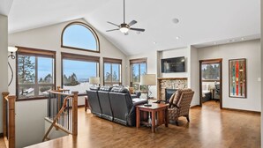Un vaste espace de vie doté d’un haut plafond, de grandes fenêtres offrant une vue sur l’extérieur, d’une cheminée et d’un coin salon avec un canapé et des fauteuils.