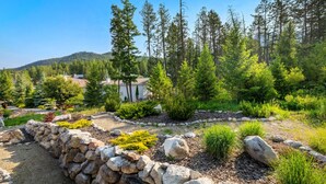 Un jardin aménagé avec un mur en pierre, divers arbustes et de grands arbres.