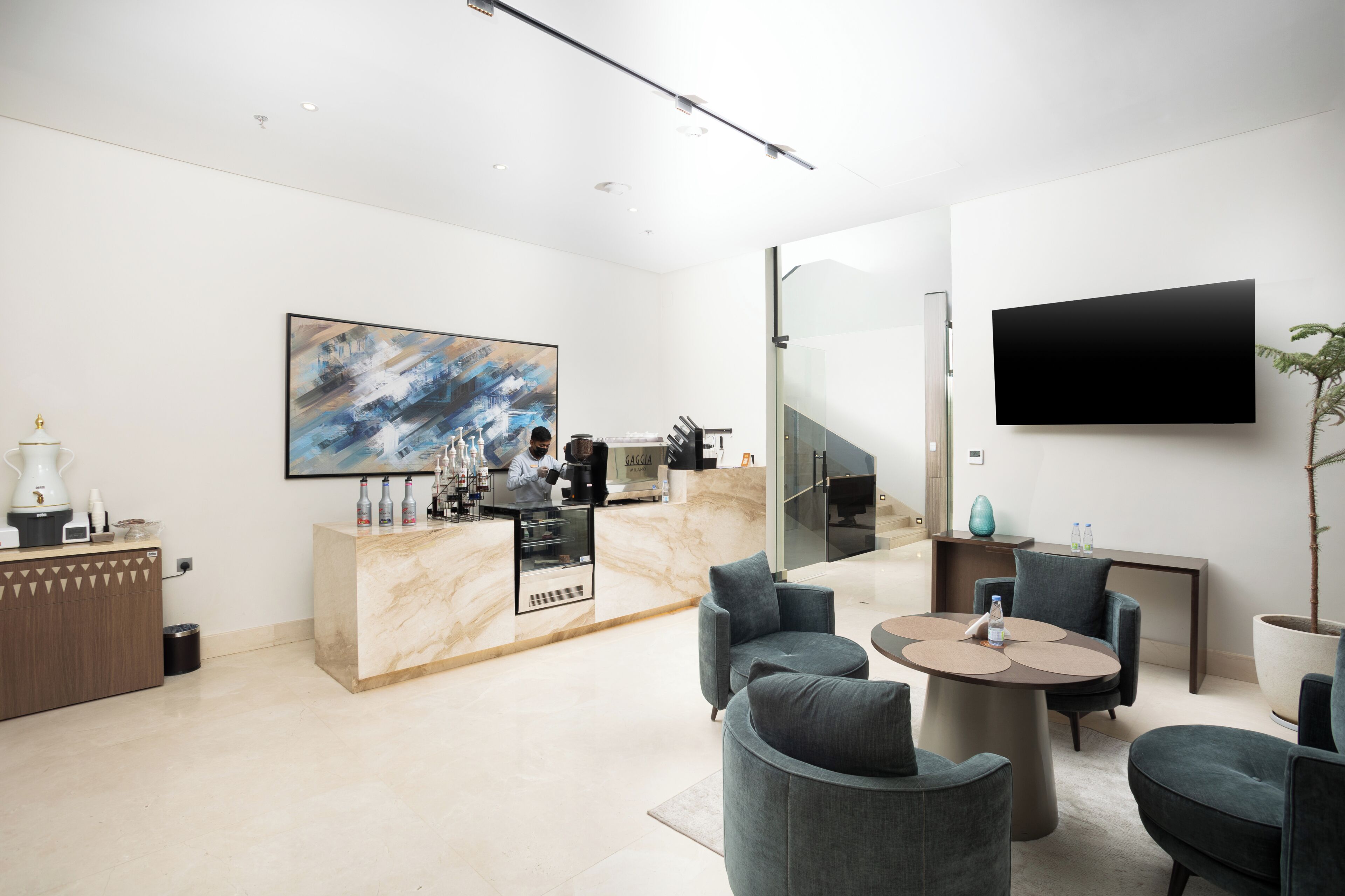 A modern hotel lobby with a marble reception desk, a large abstract painting, a flat-screen TV, and comfortable seating.