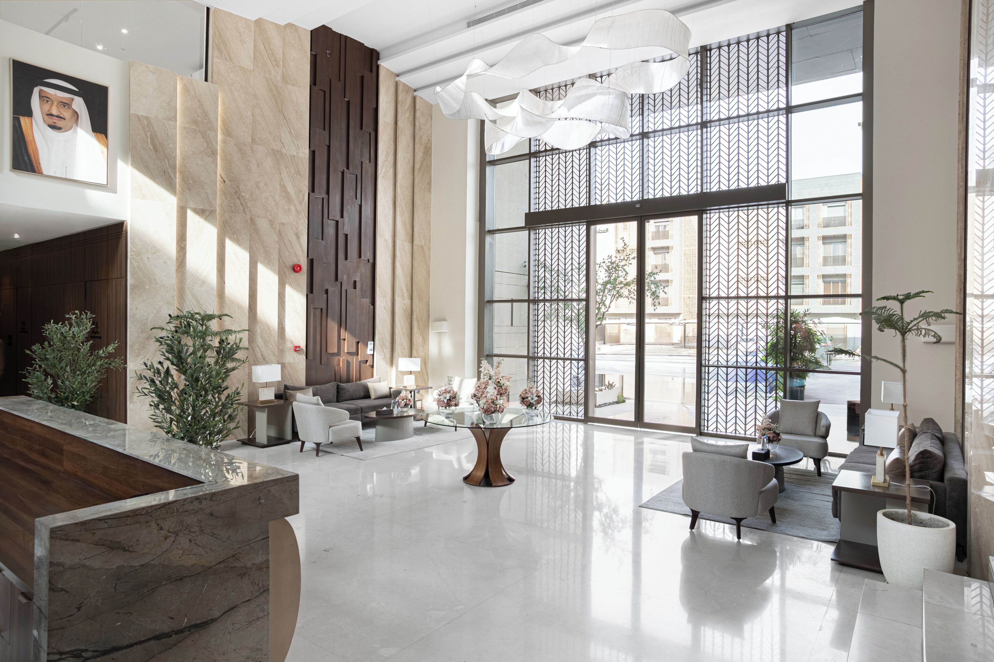 A spacious lobby with a marble reception desk, modern seating, large windows, and a decorative wall.