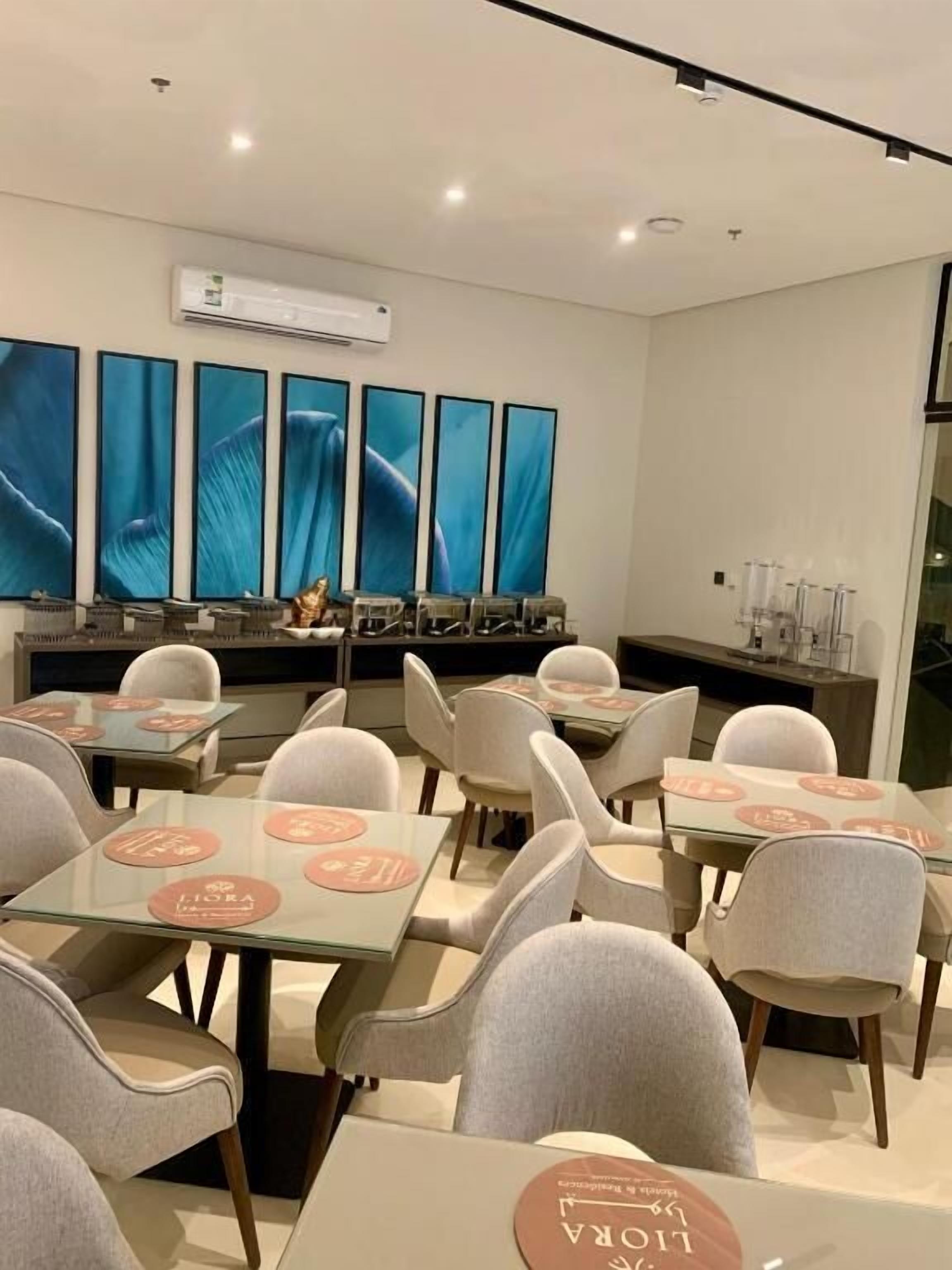 Un espace de restauration moderne, avec des tables et des chaises, un climatiseur fixé au mur et de grandes peintures abstraites.