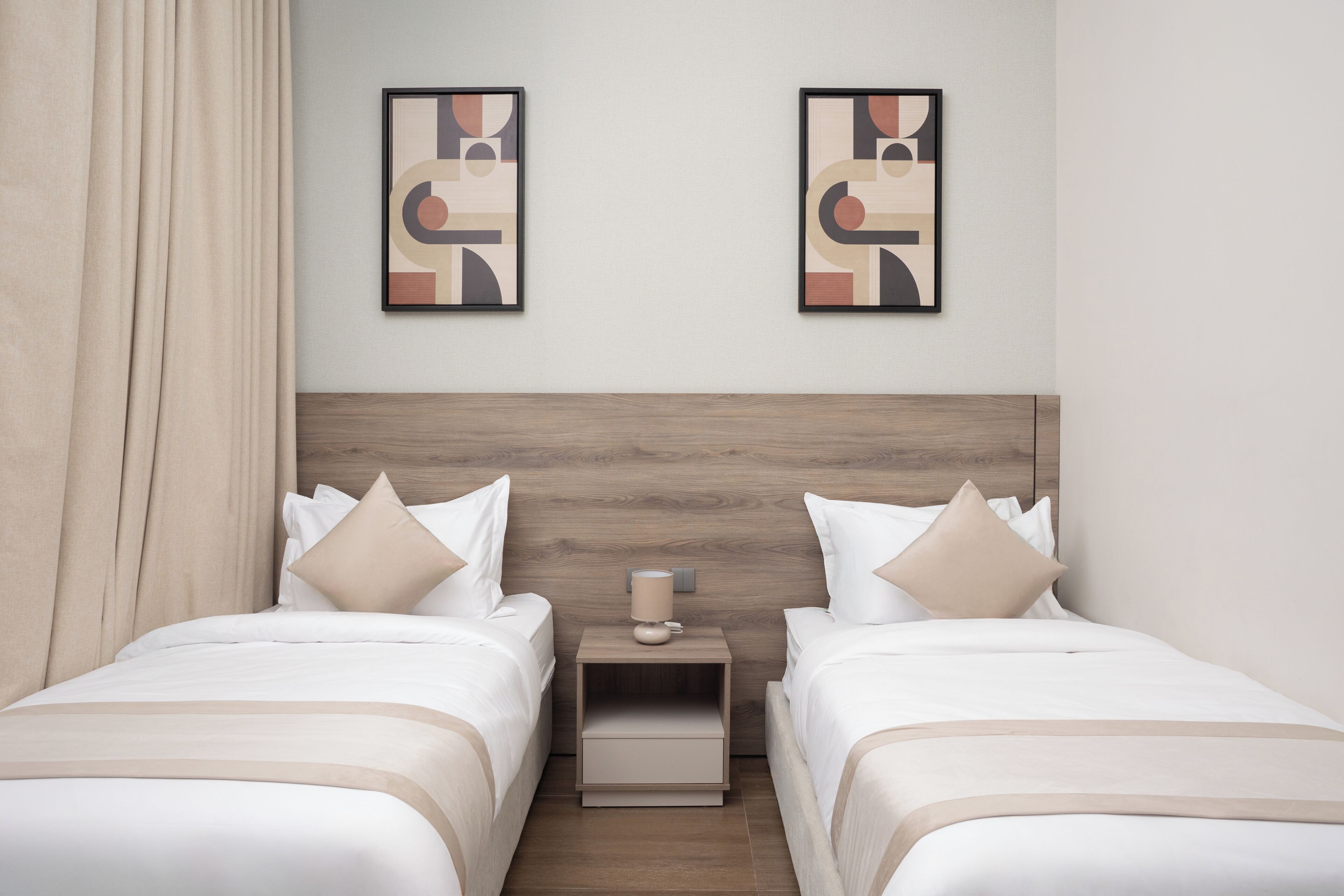 Habitació d'hotel amb dos llits, una tauleta de nit amb una làmpada i una obra d'art abstracta a la paret.