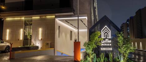 A modern building with a well-lit entrance and a signboard with the name 'MAKEEN' and a phone number.