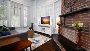 Una sala de estar con chimenea, un televisor sobre un mueble blanco y un ventanal con persianas.