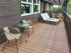 Eine Holzterrasse mit zwei Korbstühlen, einem Tisch, einer Liege und Topfpflanzen.