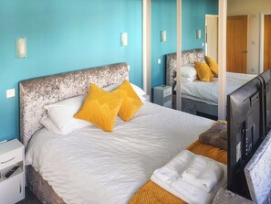 Ein Hotelzimmer mit einem großen Bett, zwei Nachttischen, einem Fernseher und einem Spiegel.