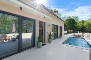 A modern house with a swimming pool, large glass doors, and outdoor furniture. - NEW Charming Villa Harmonia with Heated pool,Indoor Jacuzzi surrounded by nature (Sveta Katarina)