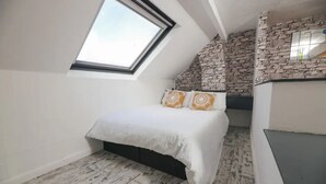 A bedroom with a skylight, a bed with patterned pillows, a stone accent wall, and a built-in wardrobe. - Frankys Place Residence in Leeds (Leeds)
