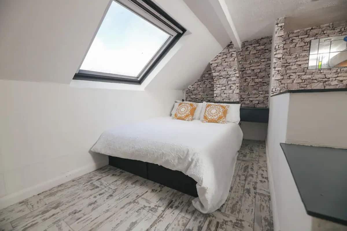 A bedroom with a skylight, a bed with patterned pillows, a stone accent wall, and a built-in wardrobe.