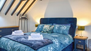 A bedroom with a large bed, a nightstand, a lamp, and a hanging rack. - Norfolk Headquarters (Fakenham)
