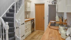 A kitchen with a wooden countertop, a washing machine, and a door leading to another room. - Norfolk Headquarters (Fakenham)