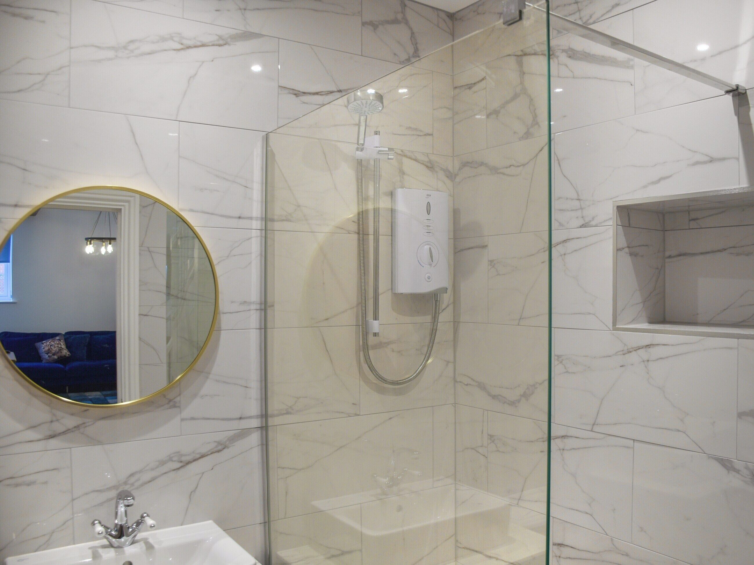 Une salle de bain moderne avec une douche à parois de verre, un miroir rond et un mur recouvert de carreaux de marbre.