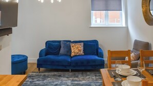 A living room with a blue sofa, a dining table set with plates and glasses, and a chandelier. - Norfolk Headquarters (Fakenham)