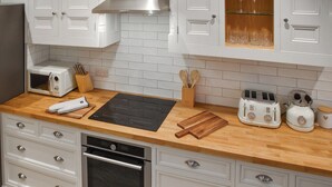 A modern kitchen with white cabinetry, a wooden countertop, a built-in oven, a microwave, a toaster, and a kettle. - Norfolk Headquarters (Fakenham)