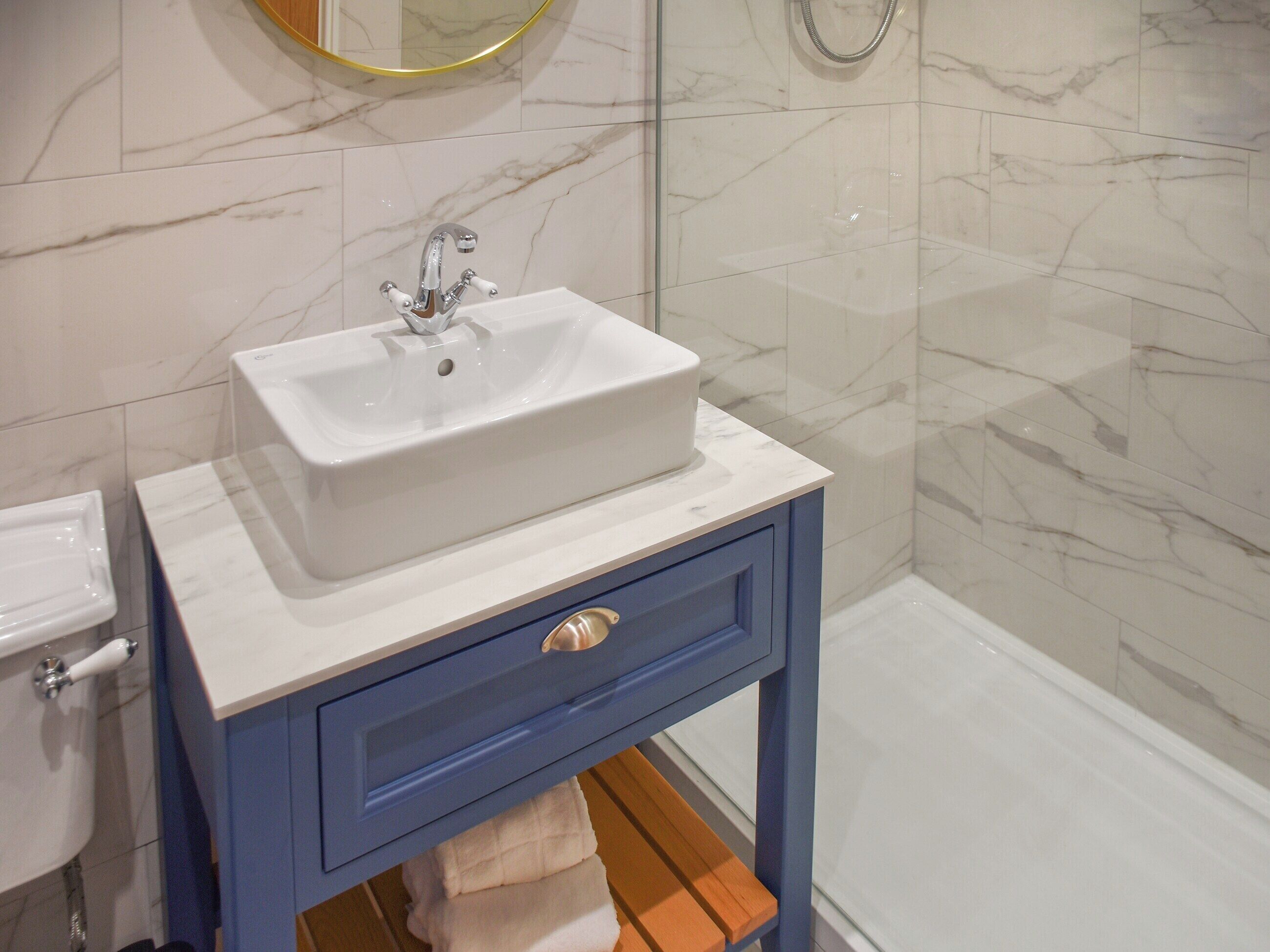 A bathroom with a white sink, blue vanity, and a glass shower enclosure.