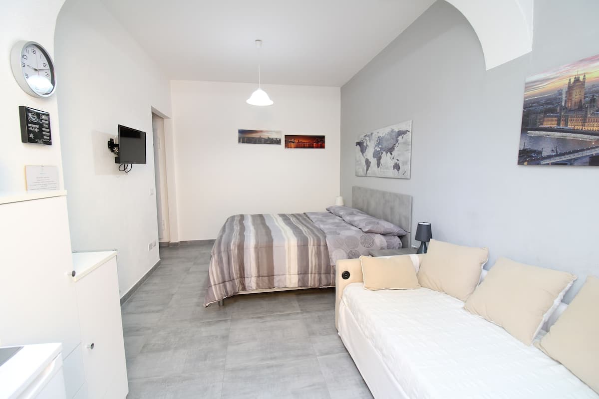 A bedroom with a bed, a sofa, a TV, and a clock on the wall.