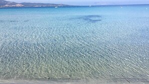 A clear, shallow sea with a sandy beach and distant buildings. - SUMMER ROOM (Siniscola)