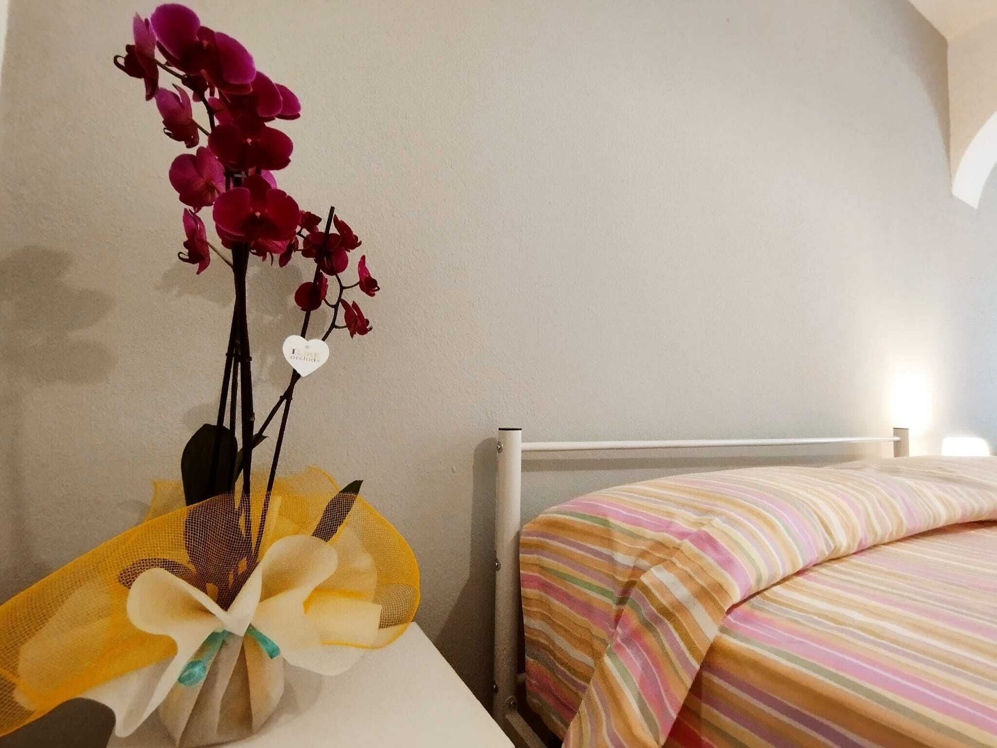 A bed with a striped bedspread, a bedside table with a vase of flowers, and a wall with a textured finish.