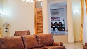 A living room with a brown leather sofa, a wooden door, and a dining area in the background. - Eey Kay Booking Ghana (Accra)
