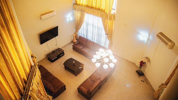 A living room with a brown sofa, a TV, a coffee table, and a massage chair. - Eey Kay Booking Ghana (Accra)
