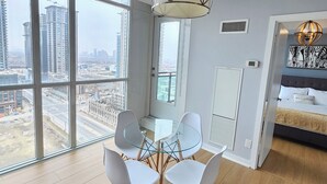 A modern hotel room with a large window, a glass table, and white chairs. - Beautiful Condo with spectacular views + 1 Parking in Mississauga Downtown (Mississauga)