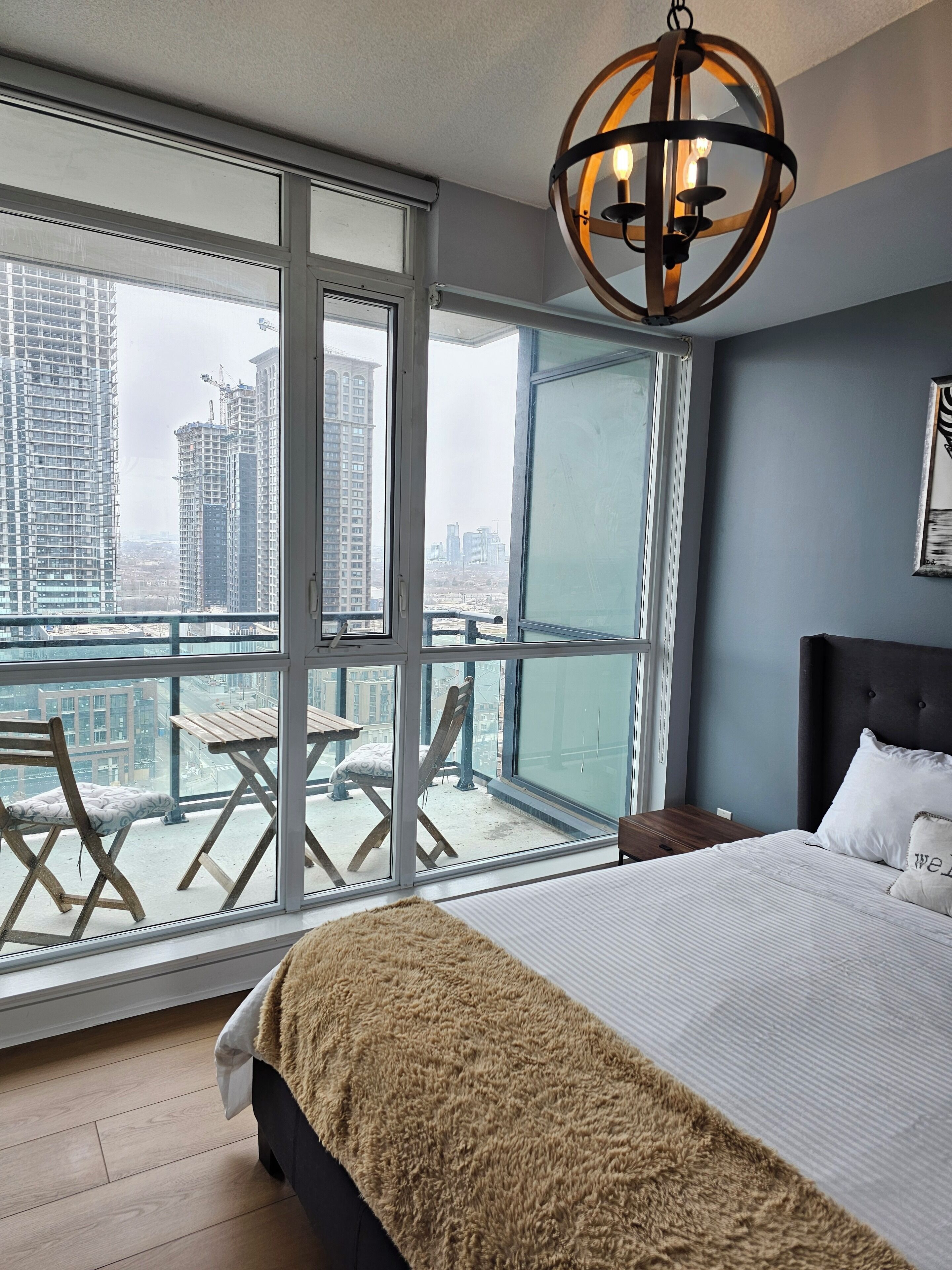 A bedroom with a large window, a bed, a nightstand, and a hanging light fixture.