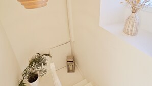 Eine Treppe mit weißer Geländer, eine hängende Holzleuchte, ein Topfpflanze und ein Fenster mit einer Vase getrockneter Blumen.
