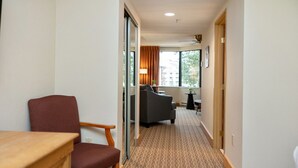 A hotel hallway with a wooden desk, a red chair, a grey sofa, and a small table with a lamp.