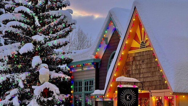 A snow-covered building with colorful lights, a sign reading "FAVOR THE KIND," and a "No Parking" sign.