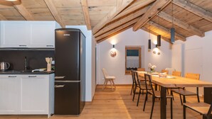 Une cuisine moderne avec un réfrigérateur noir, des poutres en bois au plafond et un coin repas comprenant une table et des chaises en bois.
