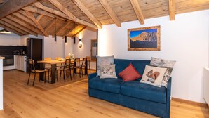 Un espace de vie moderne avec un plafond en bois, un coin repas, un canapé agrémenté de coussins décoratifs et une cuisine en arrière-plan.