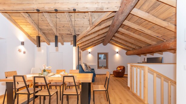 Un espace repas comprenant une table et des chaises en bois, un canapé et un escalier.