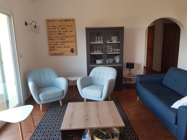 A living room with two light blue armchairs, a blue sofa, a wooden coffee table, and a cabinet with glassware.