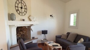 Una sala de estar con chimenea, un sofá, dos sillones, una mesita y una lámpara.