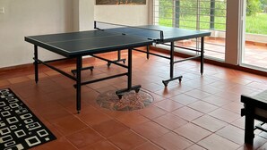 A spacious room with two ping pong tables, a large window with a view of greenery, and a ceiling with exposed beams. - Escape to paradise in Paipa, Boyacá in this beautiful Casa Rural San Cipriano!🏡 (Paipa)