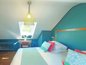 Un dormitorio con una cama, un escritorio, una silla, un radiador y una ventana.