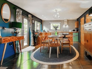 A modern kitchen with a dining area, wooden cabinets, a green refrigerator, and a chandelier.