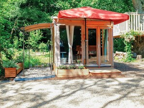 Une cabane en bois avec un toit rouge, des portes en verre et un banc à l’extérieur.
