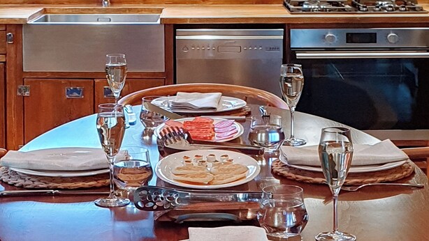 Une table à manger dressée avec des assiettes, des verres et des couverts, entourée d’une cuisine équipée d’appareils électroménagers.