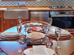 Una mesa de comedor dispuesta con platos, vasos y cubiertos, rodeada de una cocina con electrodomésticos.